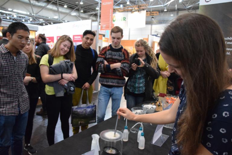 Eine Mitarbeiterin der Wangeliner Workcamps zeigt Interessent*innen am Messestand die Experimente von CRAterre. | Foto: A. Theis