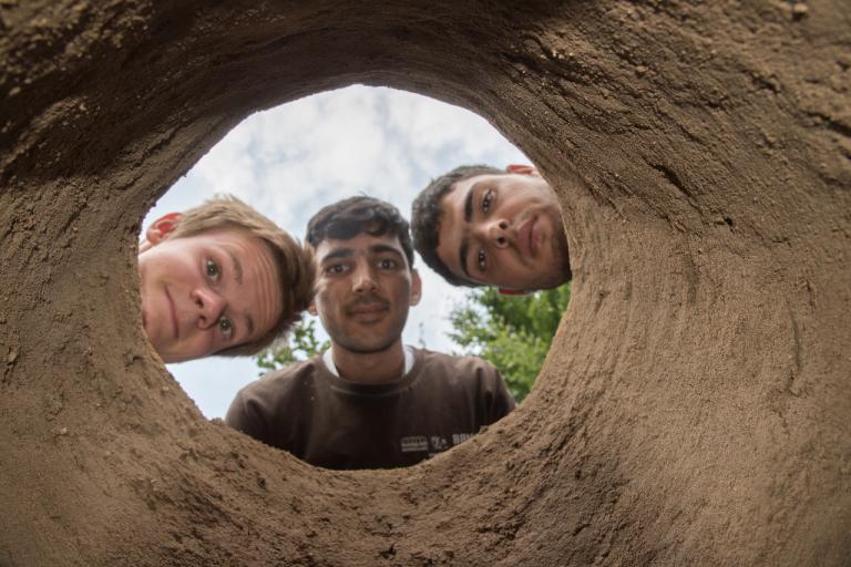 Drei Workcampteilnehmende schauen on oben in einen Tandoori Ofen, die im 'Workcamp gebaut wurde.